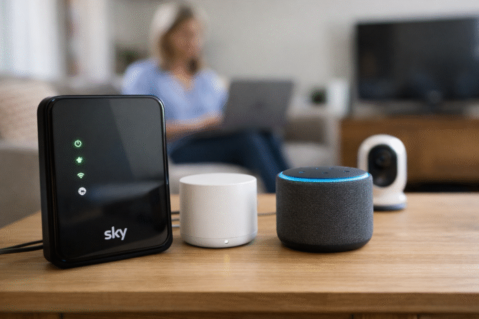 A modern home router on a table with a mesh Wi-Fi pod and a laptop in the background